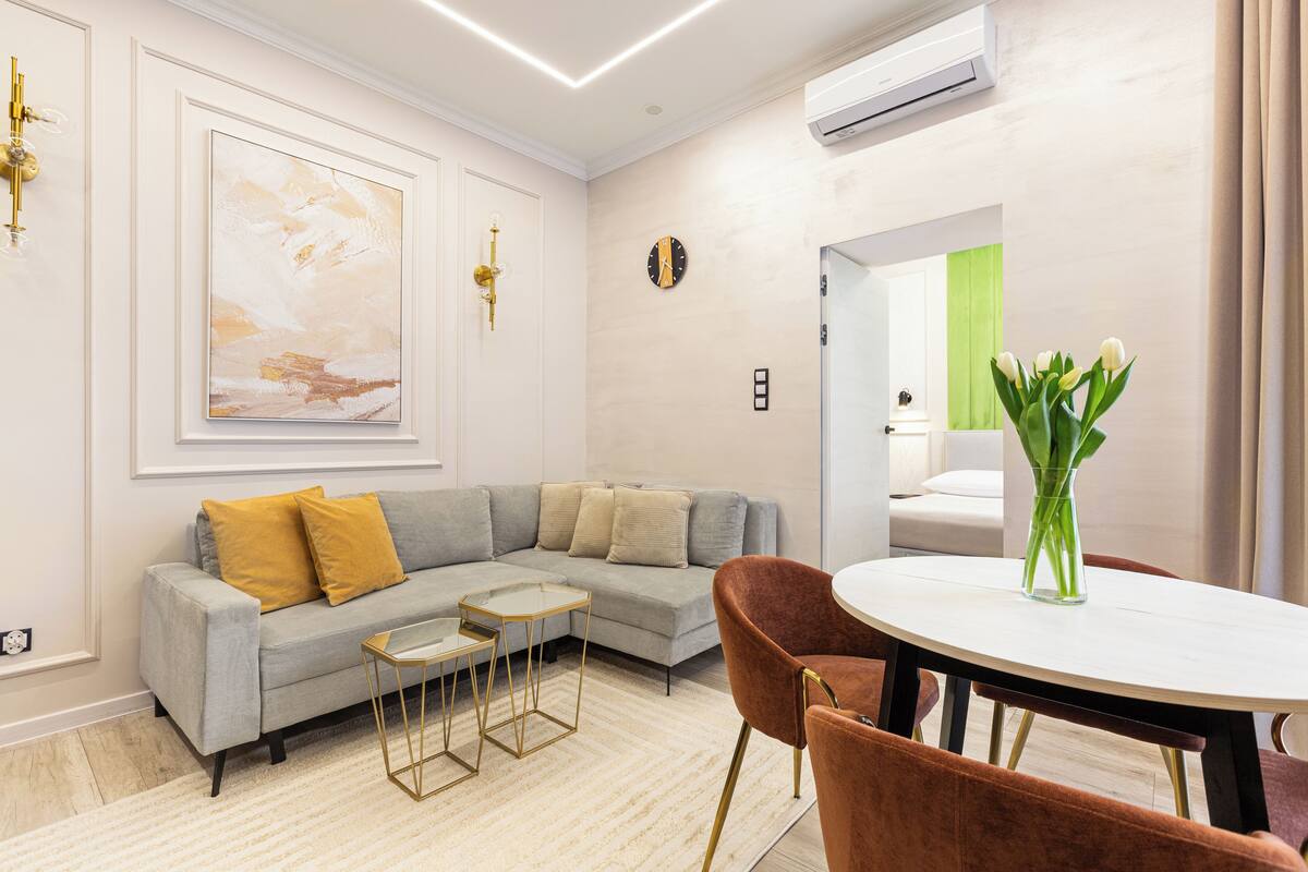 A modern living room with a grey sofa, a small coffee table, and a round table with a vase of flowers.