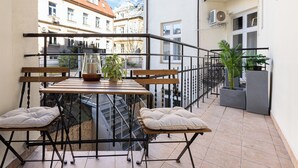 A balcony with a wooden table and two cushioned chairs, a potted plant, and a view of neighboring buildings. - Native Apartments Kołłątaja 12 (Kraków)