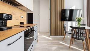 A modern kitchen with a wooden countertop, built-in appliances, and a dining area with a TV and chairs. - Native Apartments Kołłątaja 12 (Kraków)