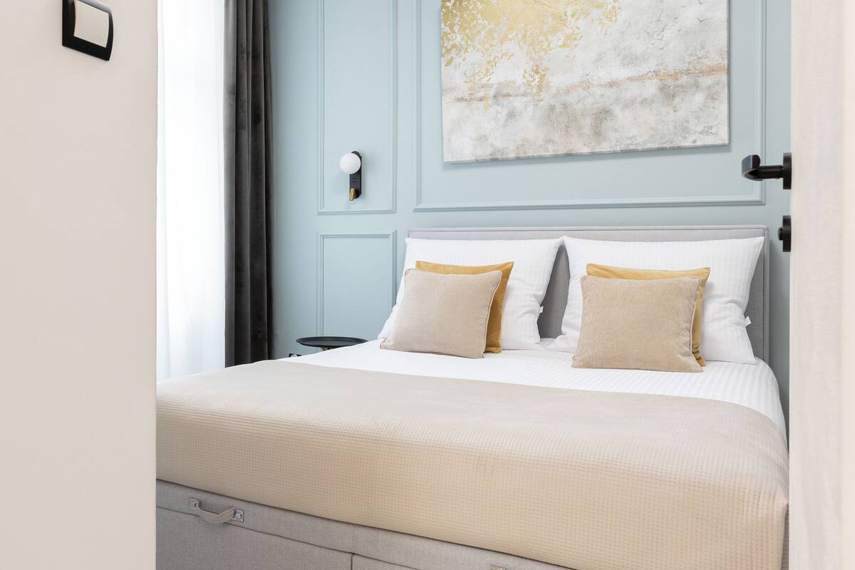 A bedroom with a bed, bedside tables, a wall-mounted light, and a window with curtains.