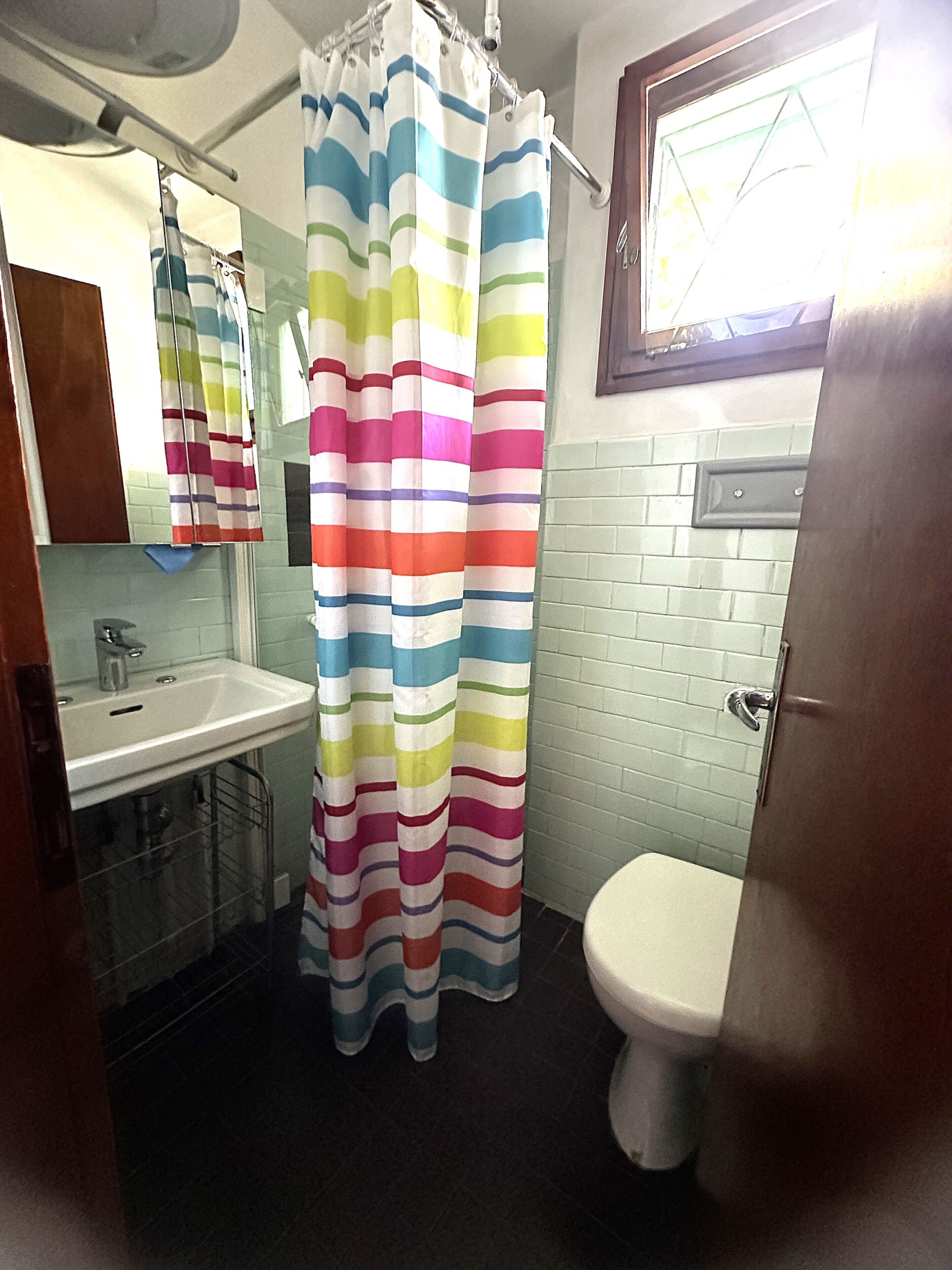 Une salle de bain avec un lavabo blanc, des toilettes et un rideau de douche à rayures multicolores.