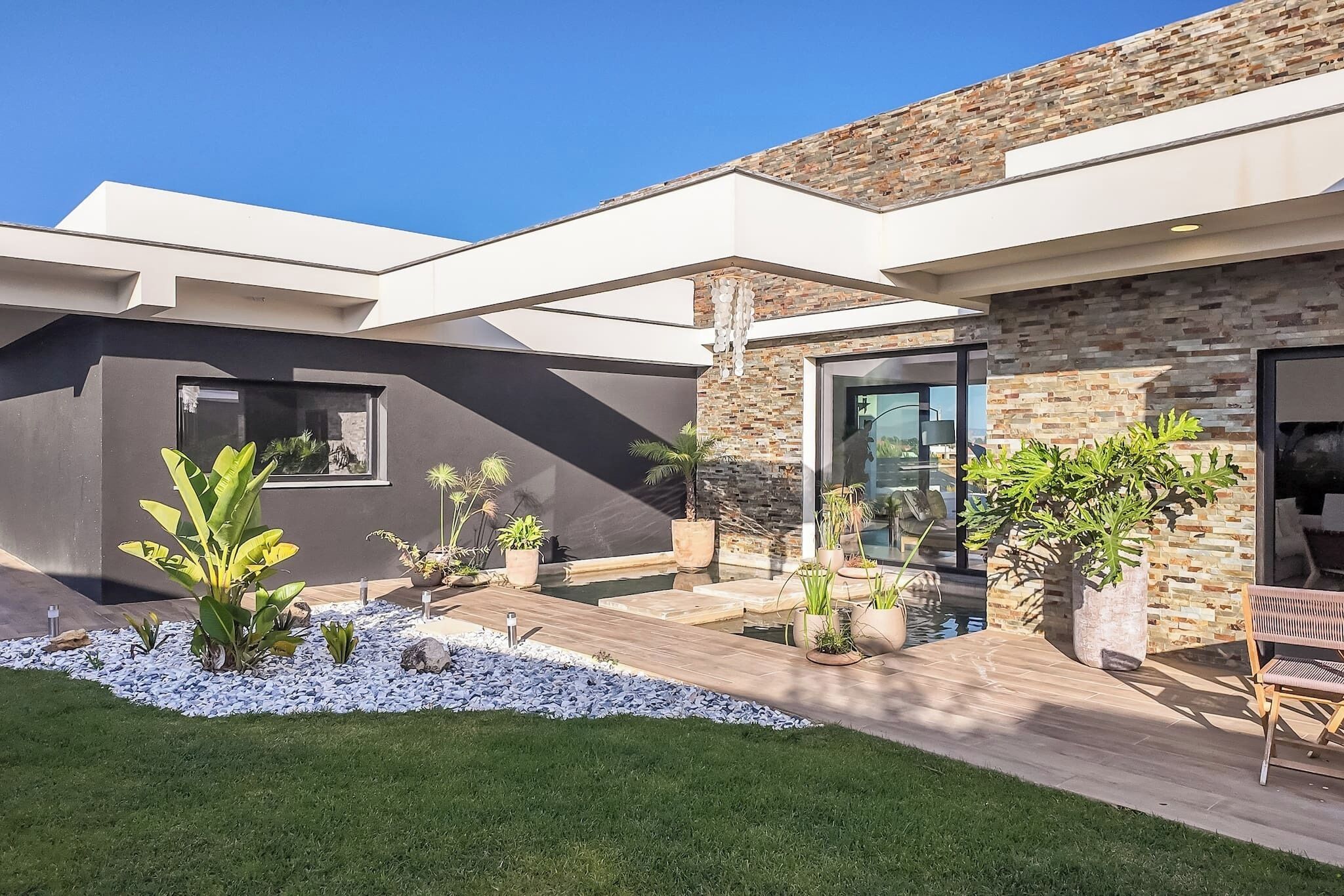 Une maison moderne dotée d’un patio, d’une piscine et de diverses plantes en pot.