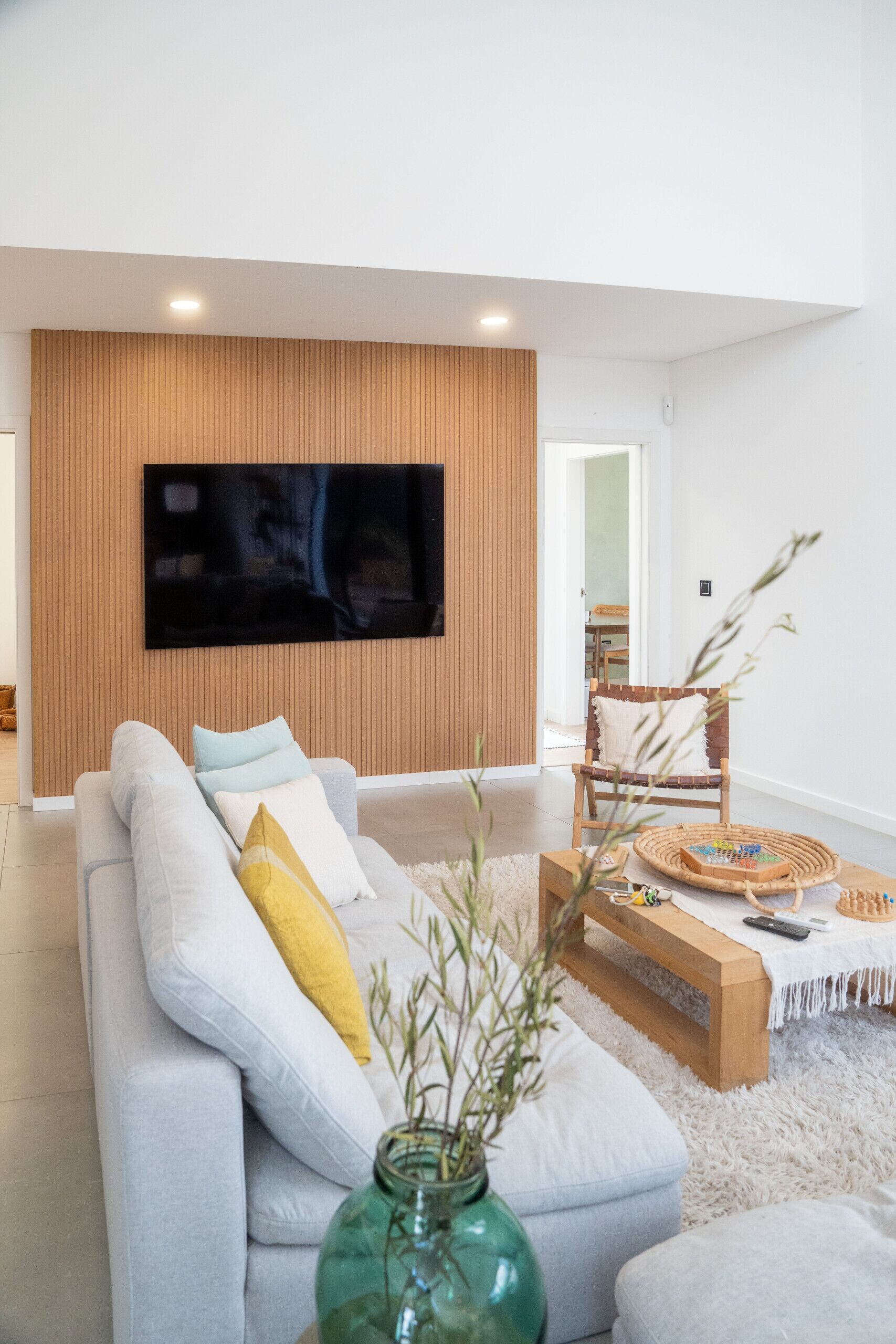 A modern living room with a sofa, a wooden accent wall, a flat-screen TV, a coffee table, and a chair.