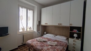 Un dormitorio con cama, ventana con cortinas, radiador, televisor y armario.
