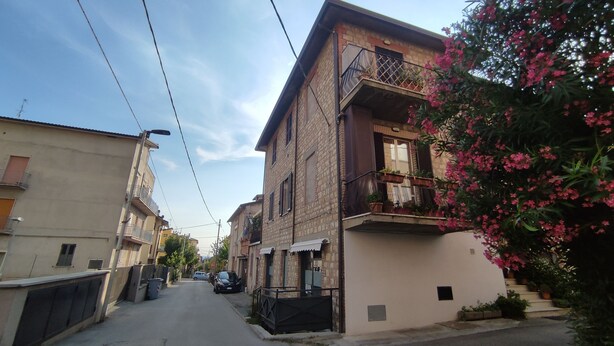 Una calle estrecha flanqueada por edificios, con balcones adornados con plantas en macetas y un cielo despejado.
