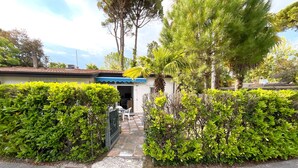 A residential property with a gated entrance, a small covered porch, and a well-maintained garden with various shrubs and trees. - Relaxing Villa With Private Garden in Nature (San Michele al Tagliamento)