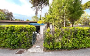 A residential property with a gated entrance, a small covered porch, and a well-maintained garden with various shrubs and trees. - Relaxing Villa With Private Garden in Nature (San Michele al Tagliamento)