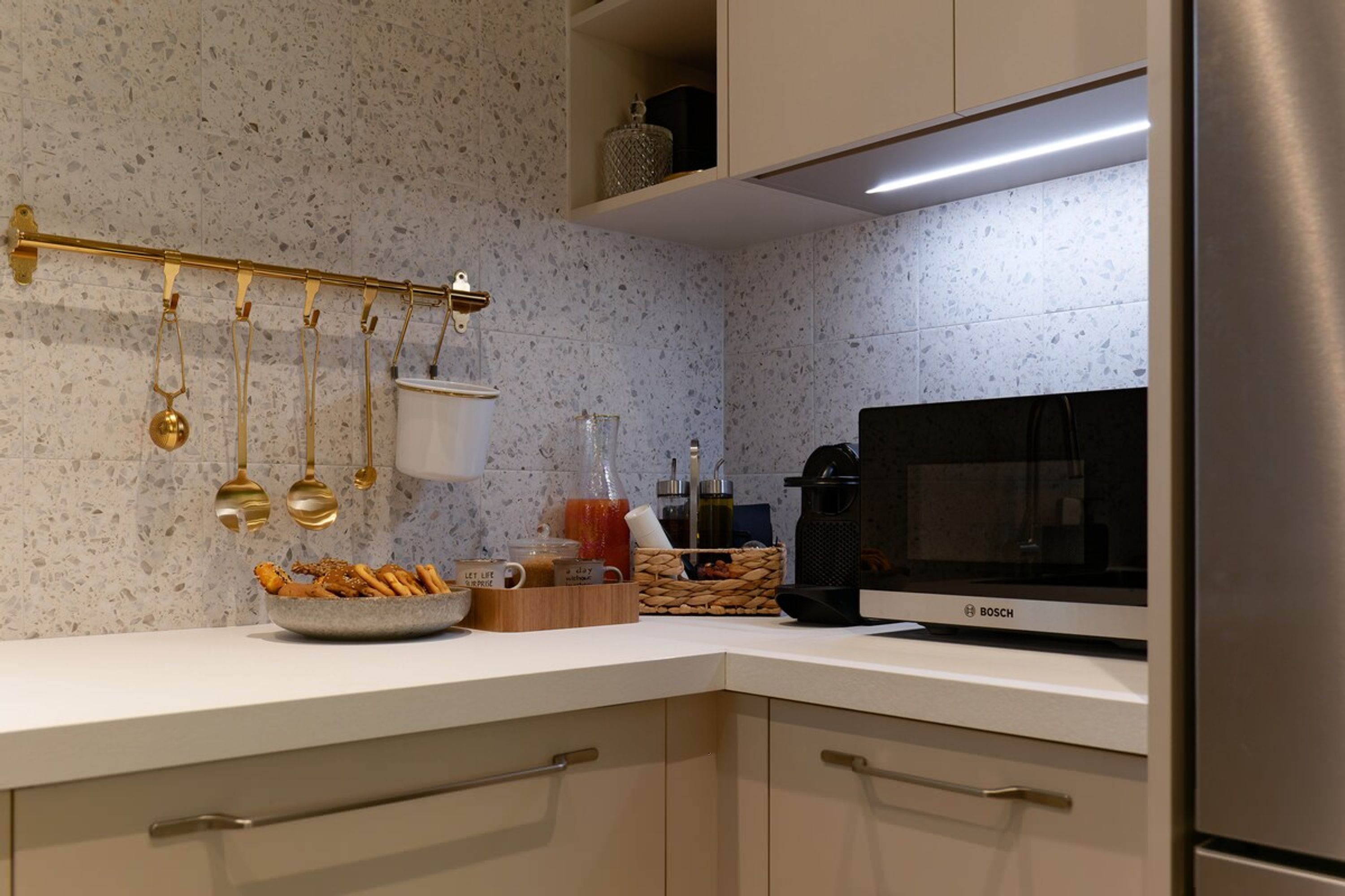 Une cuisine moderne équipée d’un four à micro-ondes Bosch, d’ustensiles suspendus, d’un panier à fruits et d’une machine à café.