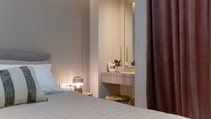 Ein modernes Hotelzimmer mit einem ordentlich bezogenen Bett, einem Nachttisch mit Lampe, einem Schminktisch mit Spiegel und einem braunen Vorhang.