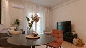 Ein modernes Wohnzimmer mit rundem Tisch, einer Couch, einem Sessel, einem Fernseher und einer Pflanze.