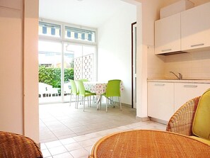 Ein Zimmer mit Essbereich, inklusive Tisch und Stühlen, einer Küche mit Schränken und Blick durch eine Glastür auf einen Sitzbereich im Freien.
