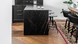 Una cocina moderna con una isla de mármol, gabinetes negros y una lámpara colgante.
