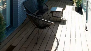 Un balcón moderno con cubierta de madera, una silla de metal negro y una mesa pequeña.