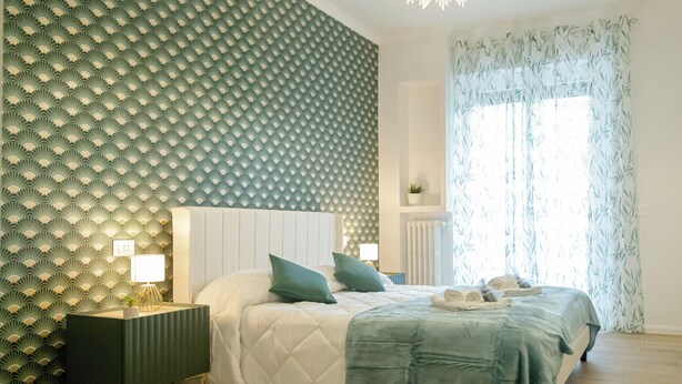 Un dormitorio ordenado con cama, mesitas de noche y una ventana con cortinas.