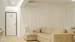 Una sala de estar moderna con un sofá seccional color beige, un radiador blanco y una puerta con letrero de prohibido fumar.