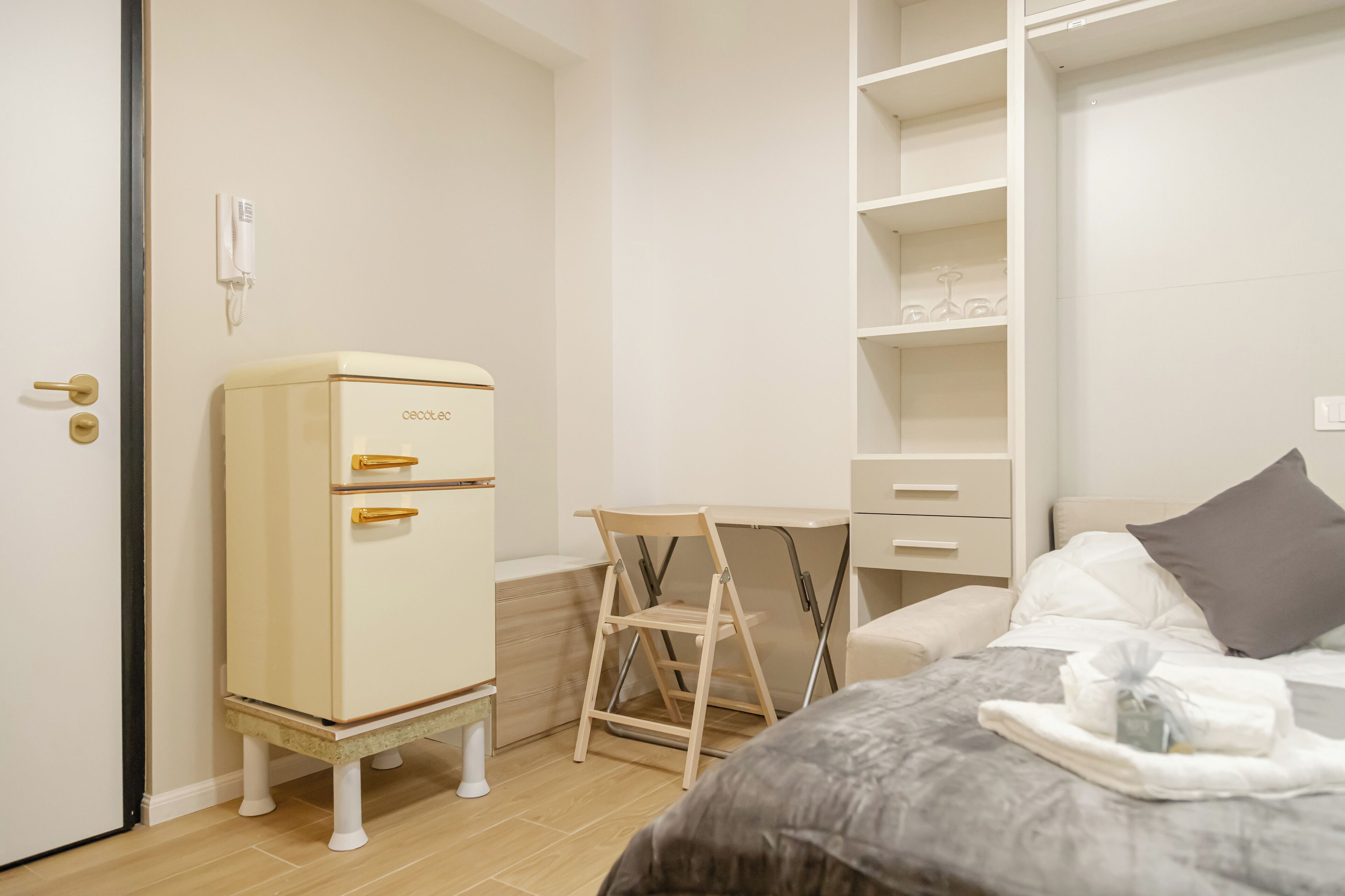 Una camera da letto con un letto, una scrivania, una sedia, un armadio e un piccolo frigorifero.