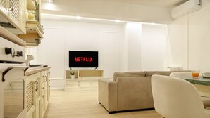 Una cocina moderna con horno empotrado, un comedor con mesa y sillas, y una pantalla grande que muestra "NETFLIX".