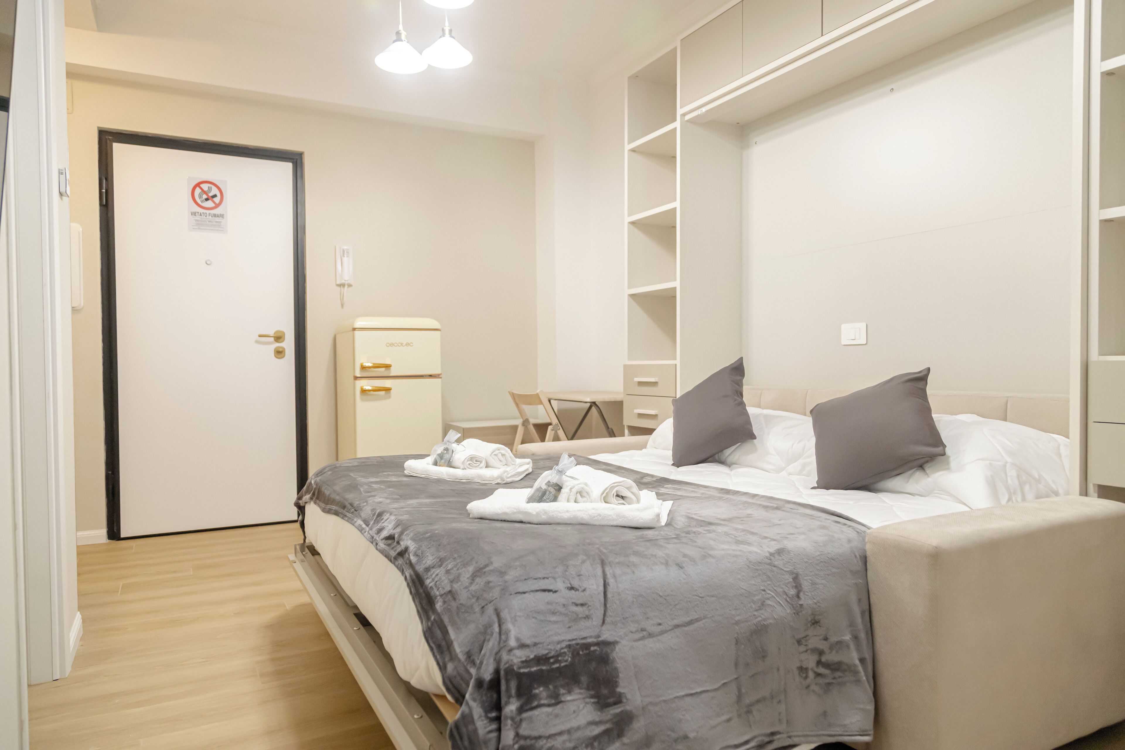 A hotel room with a bed, a desk, a chair, and a wardrobe.