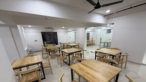 Μια σύγχρονη αίθουσα διδασκαλίας με ξύλινα τραπέζια και καρέκλες, έναν ανεμιστήρα οροφής και ένα μεγάλο παράθυρο.