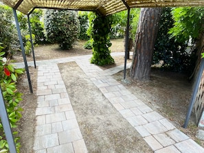 A garden pathway with a pergola structure, surrounded by various plants and trees. - Holiday Villa With Private Garden Close to the sea (San Michele al Tagliamento)