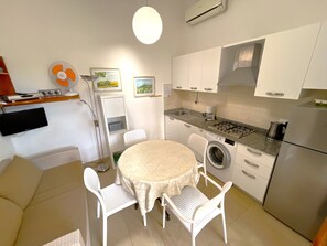 A compact kitchen with a round table, chairs, a washing machine, and a refrigerator. - Holiday Villa With Private Garden Close to the sea (San Michele al Tagliamento)