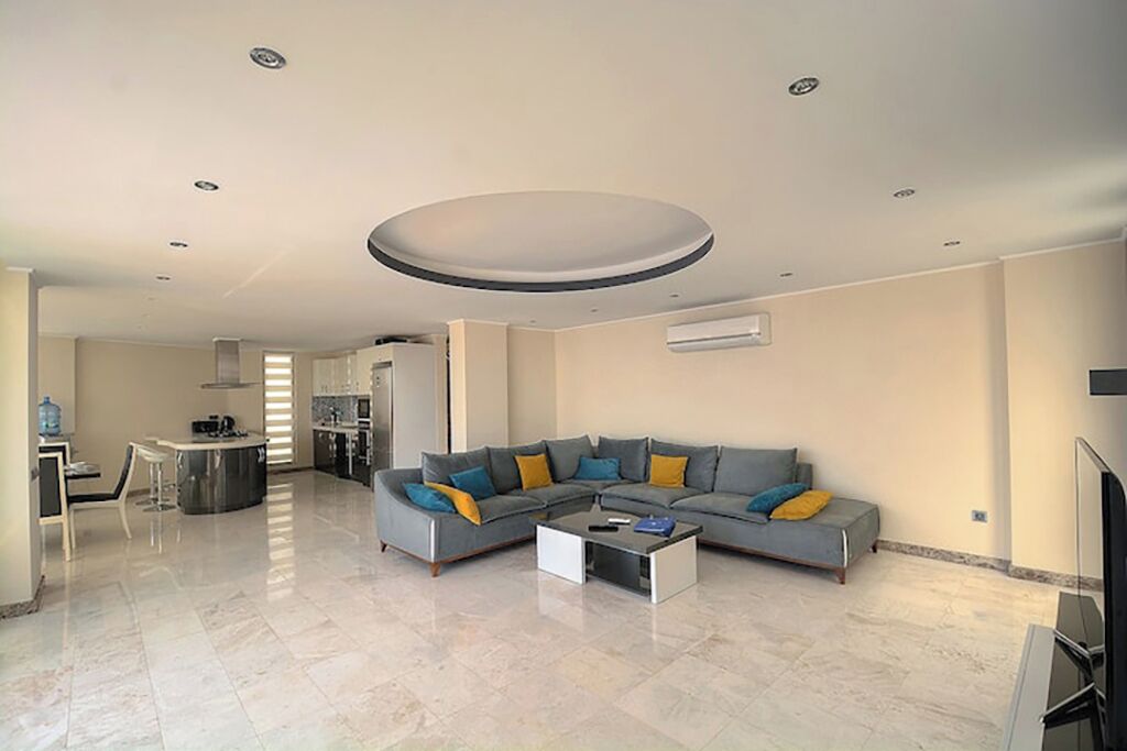Una sala moderna con un sofá seccional, una mesa de centro y una zona de cocina al fondo.