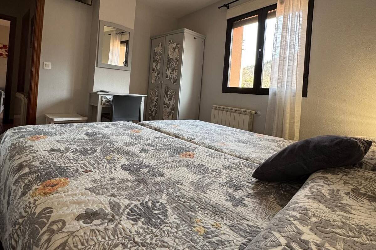 Un dormitorio con cama, escritorio, armario y ventana con cortinas.