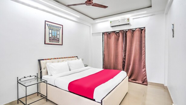 A neatly arranged bedroom with a bed, a ceiling fan, an air conditioning unit, and a framed picture on the wall.