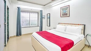 A hotel room with a bed, a ceiling fan, a window with curtains, and a framed picture on the wall.