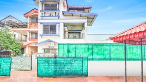 A multi-story residential building with a flat roof, a balcony on the second floor, and a green gate in front.