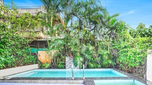A swimming pool surrounded by lush greenery and a stone wall. - Villa Bliss by Palette Homes (Mawal)