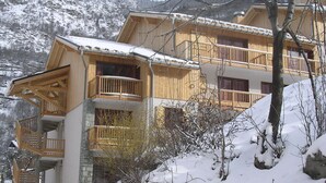 A wooden chalet with multiple balconies, set against a snowy mountainous backdrop. - Apartment in Orelle Near 3 Vallees Ski Area (Orelle)