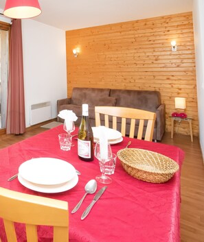 A dining area with a red tablecloth, wooden chairs, a bottle of wine, glasses, and a basket. - Apartment in Orelle Near 3 Vallees Ski Area (Orelle)