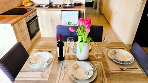 Comedor con mesa lista para dos personas, un jarrón de flores y una botella de vino.