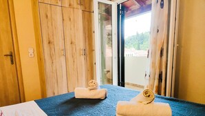 Una habitación con cama, dos toallas enrolladas, paredes de madera y vistas a través de un ventanal.