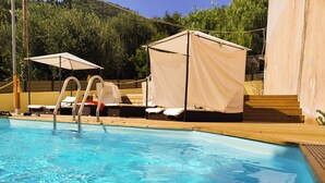 Una piscina con muelle de madera, sillas de descanso y zona de estar cubierta.