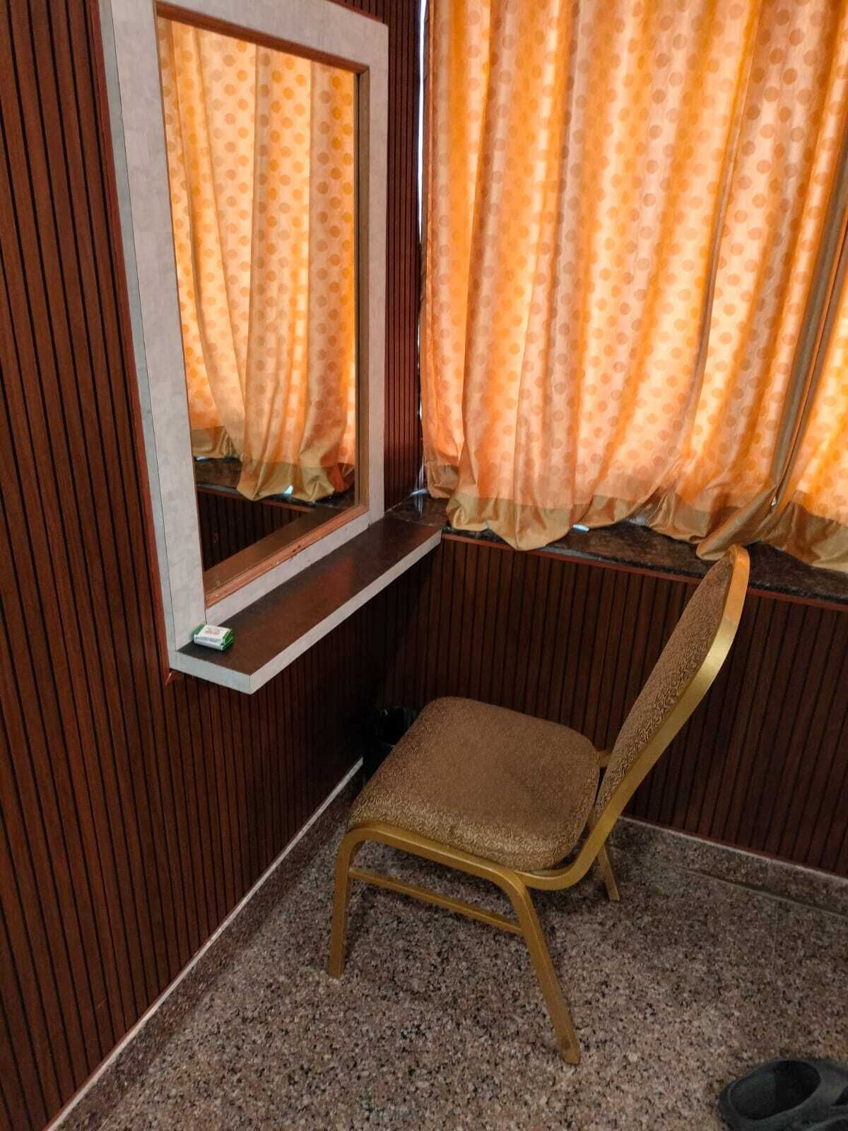 A room with a wooden paneled wall, a window with orange curtains, a small wooden bench, and a mirror.