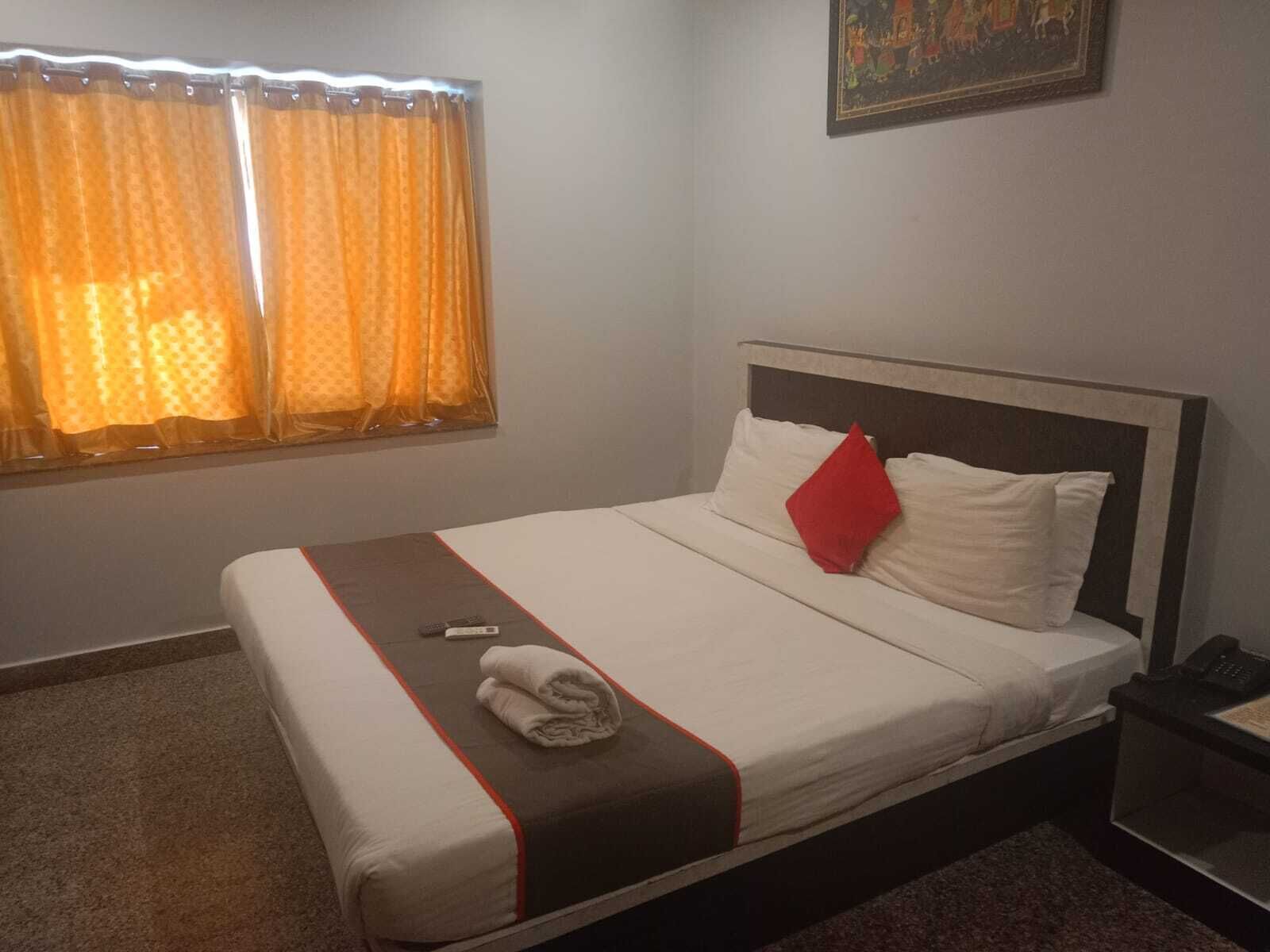 A neatly made bed with a white and brown bedspread, a red pillow, and a folded towel.