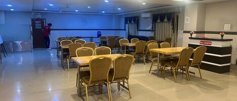 A spacious dining area with multiple tables and chairs, a bill counter, and ceiling fans.
