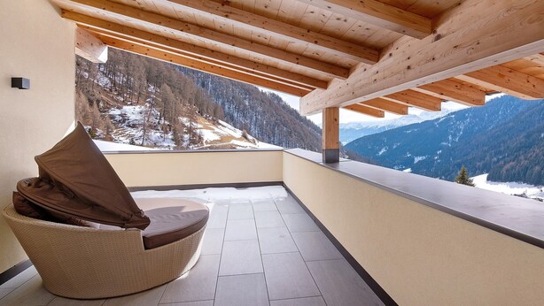 Ein Balkon mit Korbstuhl und Blick auf schneebedeckte Berge.