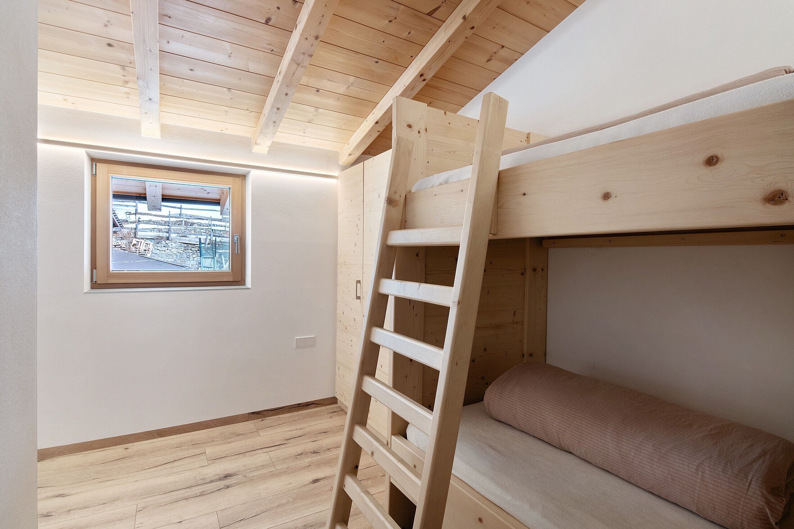Una cama litera con escalera de madera, una ventana con vistas y suelo de madera.