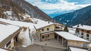 Ein Bergort mit schneebedeckten Dächern, einer Seilbahn und Blick auf verschneite Berge.