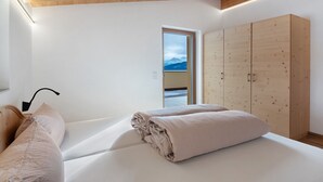 Ein Schlafzimmer mit Bett, Kleiderschrank und Blick auf Berge durch eine Tür.