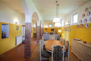 A dining area with a round table, chairs, a brick column, and a wall with plates. - Anemone - Characteristic farmhouse (Poggio delle Corti)