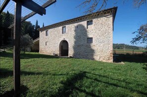 A stone building with a central archway, surrounded by a grassy area and trees. - Anemone - Characteristic farmhouse (Poggio delle Corti)