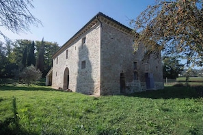 Ein Gebäude aus Stein mit flachem Dach und Rundbogenfenstern, umgeben von Gras und Bäumen.