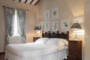 Ein Schlafzimmer mit einem Bett, zwei Nachttischen mit Lampen, einer Kommode und botanischen Wandbildern.
