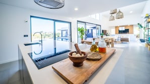 A modern kitchen with a large island, a built-in stove, and a wooden bowl with a mortar and pestle. - Setubal Lisbon Dream Getaway Villa do Sol (Seixal)