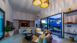 A modern living room with a sofa, coffee table, and a large window offering a view of the outdoors. - Setubal Lisbon Dream Getaway Villa do Sol (Seixal)