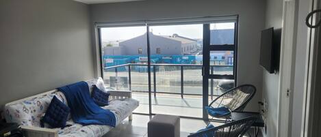 A modern living room with a sofa, a small table, and a chair. A large window offers a view of the outside.